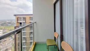 Un balcón con piso verde, dos sillas de mimbre y vista a un paisaje urbano.