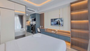 Habitación de hotel moderna con una cama grande, televisor montado en la pared, minibar y zona de estar con vistas a la ciudad.