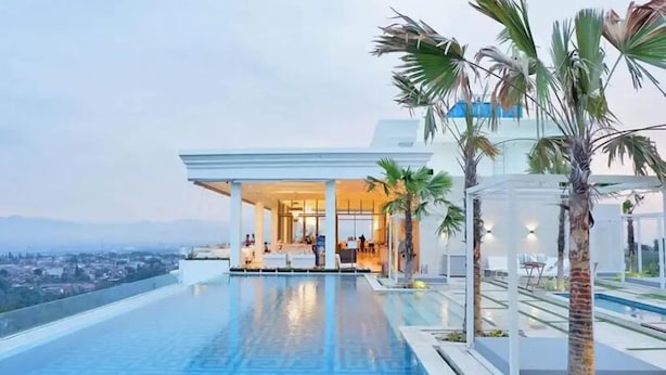 A modern hotel with a rooftop infinity pool, palm trees, and a city view. - Minimalist Look Studio Apartment At Art Deco (Bandung)