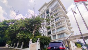 A multi-story building with balconies, a car parked in front, and a flag on top. - Minimalist Look Studio Apartment At Art Deco (Bandung)