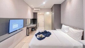A modern hotel room with a bed, a flat-screen TV, a desk, and a bathroom. - Minimalist Look Studio Apartment At Art Deco (Bandung)