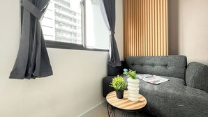 A modern living room with a grey sofa, a round wooden table with a plant, and a window with curtains. - Studio Near Kalideres Station At Daan Mogot City Apartment (Jakarta)