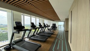 A gym with treadmills aligned along a wall with large windows offering a city view. - Stylish Studio Apartment At The Smith Alam Sutera (Tangerang)