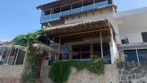 A two-story building with a thatched roof over the entrance and a stone wall with greenery.