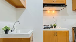 A kitchen with wooden cabinets, a white countertop, a sink, a stove, and a small potted plant. - 2Br Near Lrt Station At Signature Park Grande Apartment (Jakarta)