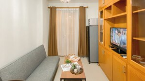 A living room with a grey sofa, a wooden cabinet with a television, and a small table with magazines and a plant. - 2Br Near Lrt Station At Signature Park Grande Apartment (Jakarta)