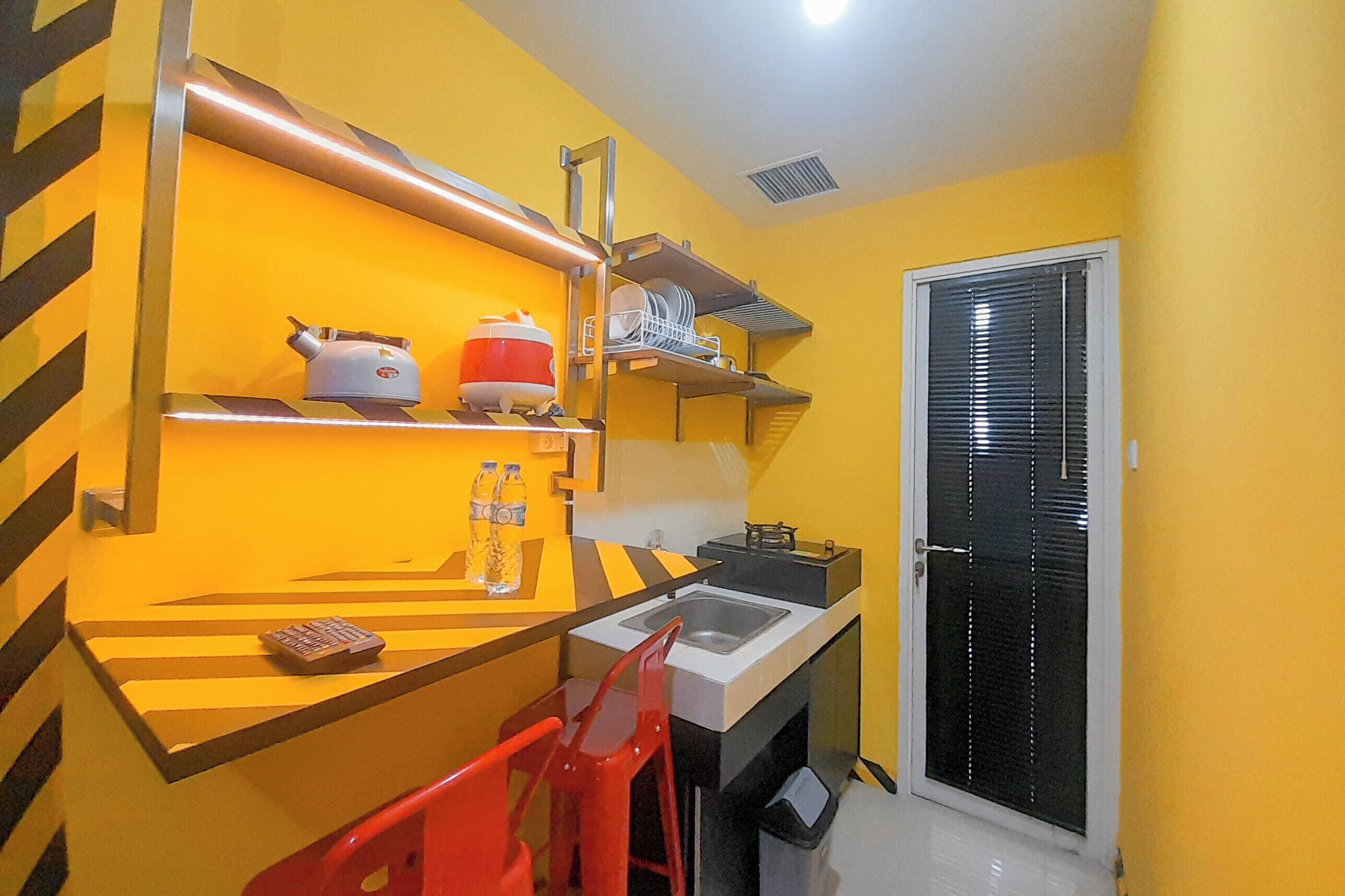 A compact kitchen with a sink, a red chair, and shelves holding kitchenware.