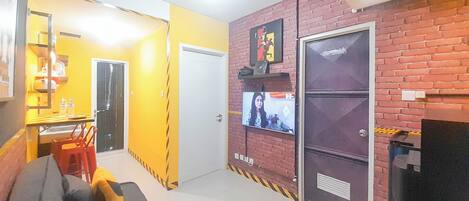 A living room with a sofa, a TV mounted on a brick wall, and a dining area with a table and chairs.