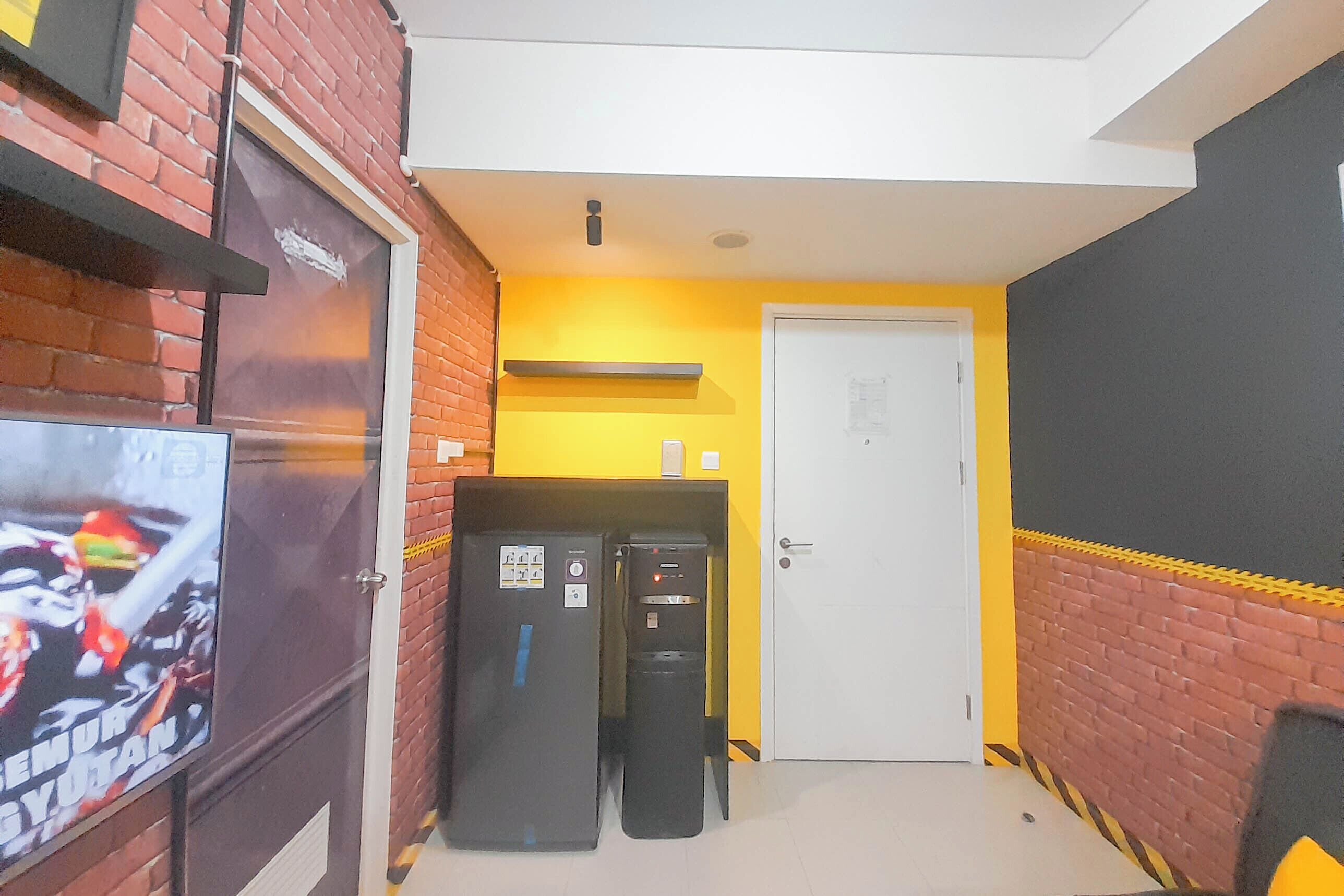 Un pasillo estrecho con un televisor a la izquierda, un refrigerador y un cubo de basura en el centro, y una puerta al final.
