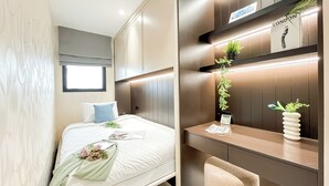 A modern hotel room with a neatly made bed, a small desk with a plant, and a wall-mounted shelf with a sign reading "LONDON". - Stylish And Modern 2Br At Apartment Collins Boulevard (Tangerang)
