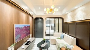 A modern hotel lobby with a wooden wall, a large painting, a black coffee table, a sofa with cushions, and a chandelier. - Stylish And Modern 2Br At Apartment Collins Boulevard (Tangerang)