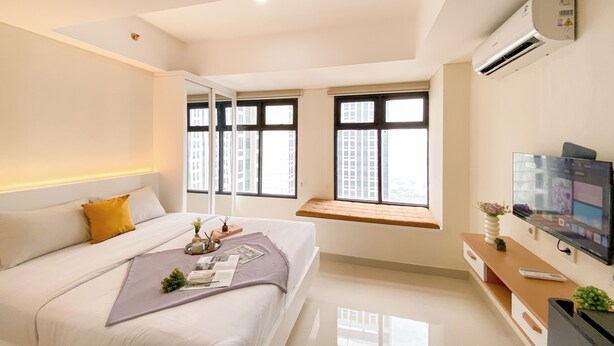 A modern bedroom with a bed, bedside table, TV, and large windows. - Studio With Direct Access Mall At Pollux Chadstone Apartment (Cikarang)