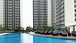 A swimming pool with lounge chairs and tall buildings in the background. - Studio With Direct Access Mall At Pollux Chadstone Apartment (Cikarang)