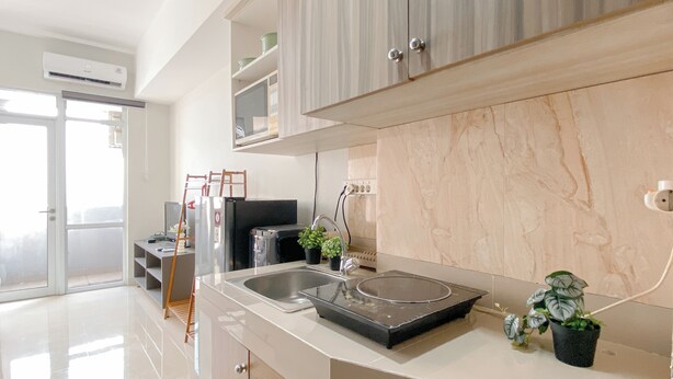 Una cocina moderna con un lavamanos de acero inoxidable, estufa integrada y salpicadero de mármol. Se observa una escalera de madera apoyada en la pared y una planta en maceta sobre la encimera.