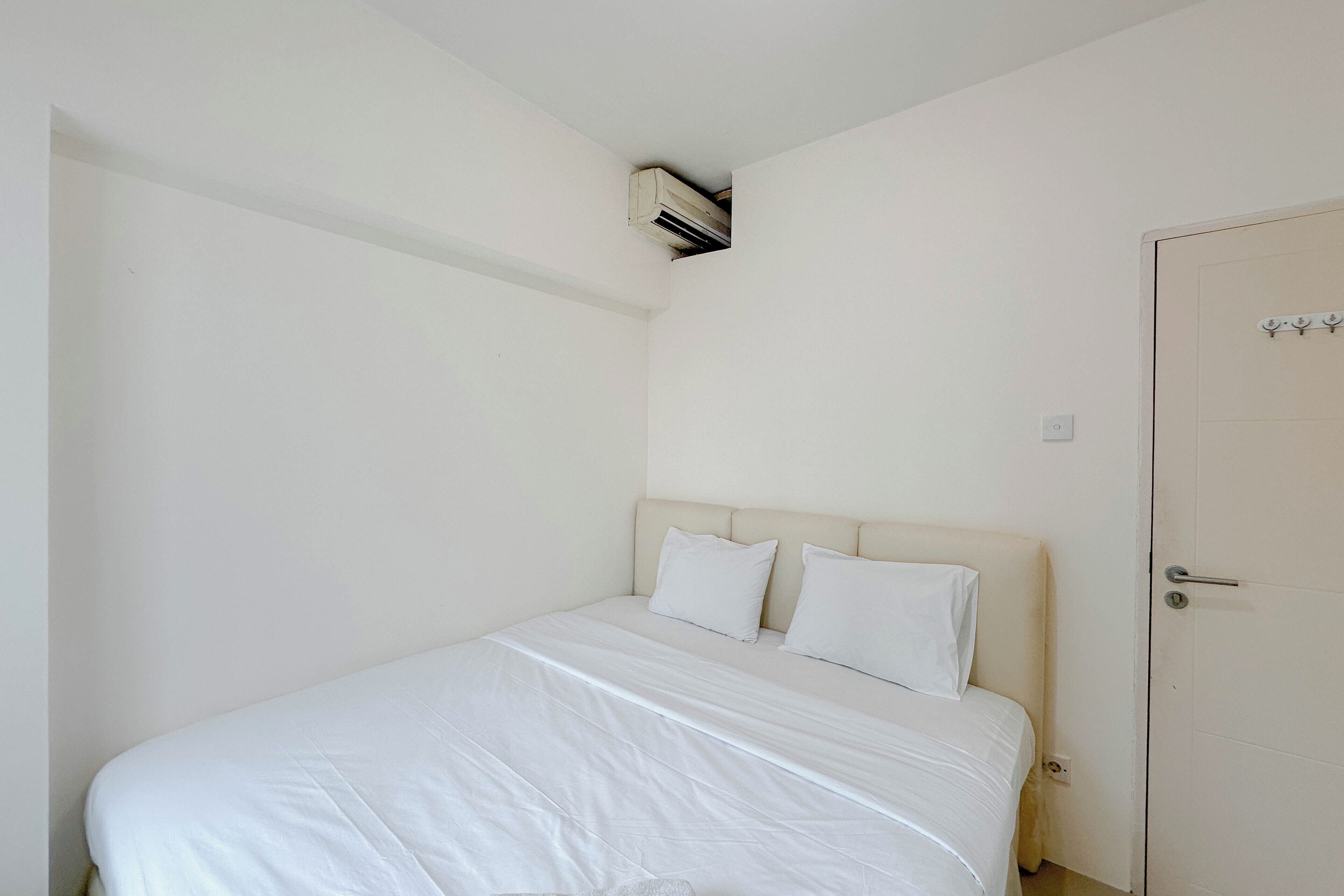 A bedroom with a bed, a door, and an air conditioning unit.
