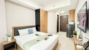 A modern hotel room with a large bed, a wooden wardrobe, a television, and a desk with a plant.