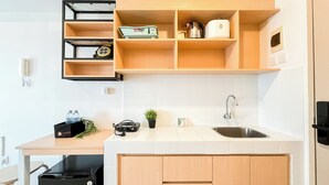 A modern kitchen with wooden cabinets, a stainless steel sink, and a built-in shelf unit. - Studio Basic Apartment At Tokyo Riverside Pik 2 (Teluknaga)