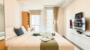 A hotel room with a bed, a TV, a bookshelf, and a window with curtains. - Studio Basic Apartment At Tokyo Riverside Pik 2 (Teluknaga)