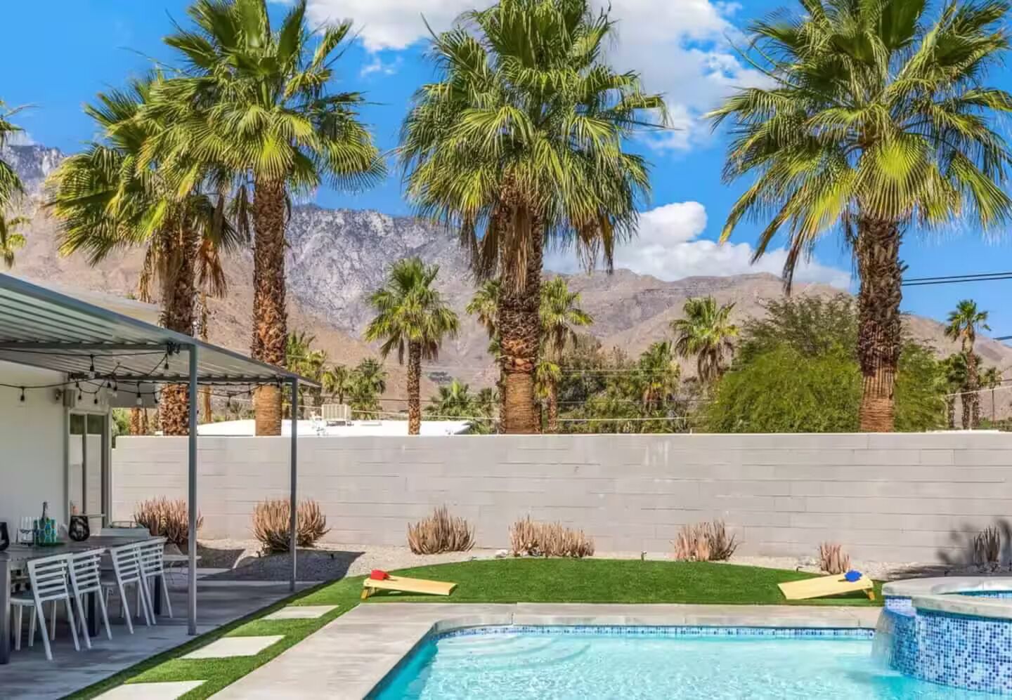 A backyard with a swimming pool, palm trees, and a mountain backdrop.