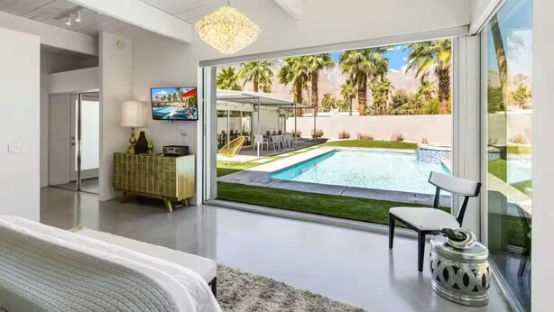 Ein modernes Wohnzimmer mit einem großen Schiebeglastür, die zu einem Poolbereich führt, einem Fernseher und einem grünen Schrank.