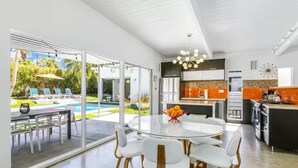 Eine moderne Küche mit Kochinsel, einem Essbereich mit Glastisch und Blick auf Pool und Garten.