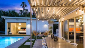Eine moderne Außenpatio mit Pool, Essbereich mit Stühlen und Feuerstelle.