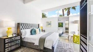 Ein modernes Schlafzimmer mit einem gesteppten Kopfteil, einem großen Bett, einem Nachttisch mit Lampe und Blick ins Freie.