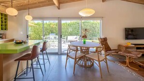 Een moderne keuken met een groen aanrecht, houten balken in het plafond en een eetgedeelte met rieten stoelen en een ronde tafel.