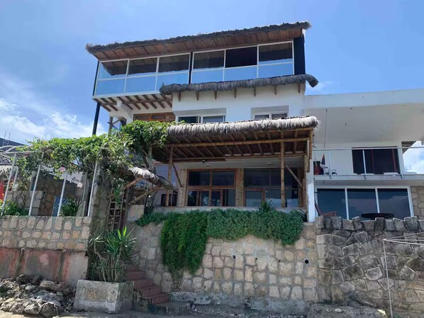 A two-story building with a thatched roof over the entrance, stone walls, and a staircase leading to the upper floor.