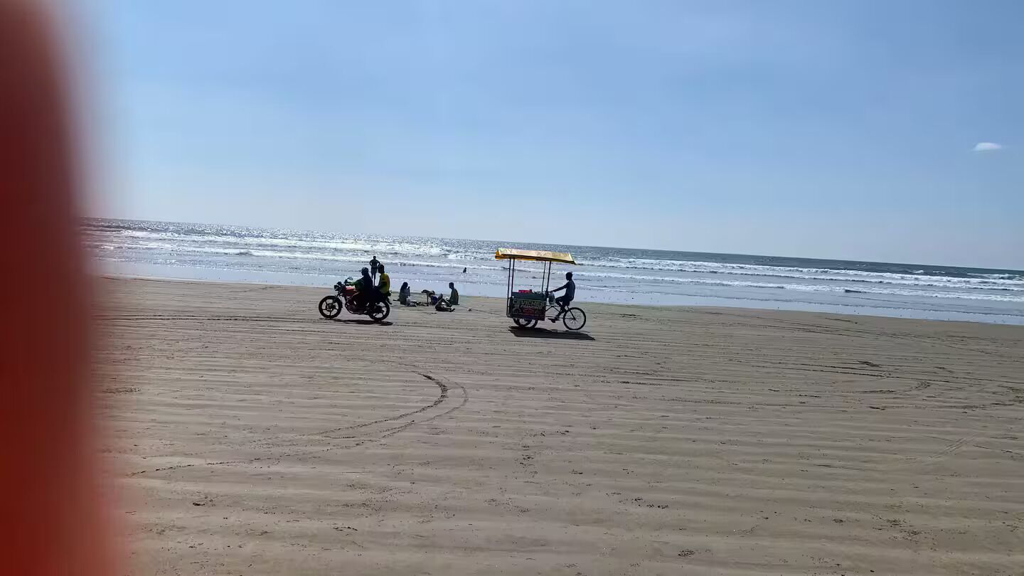 Ein Strand mit blauem Himmel, sandigem Ufer und einigen Personen sowie Fahrzeugen.