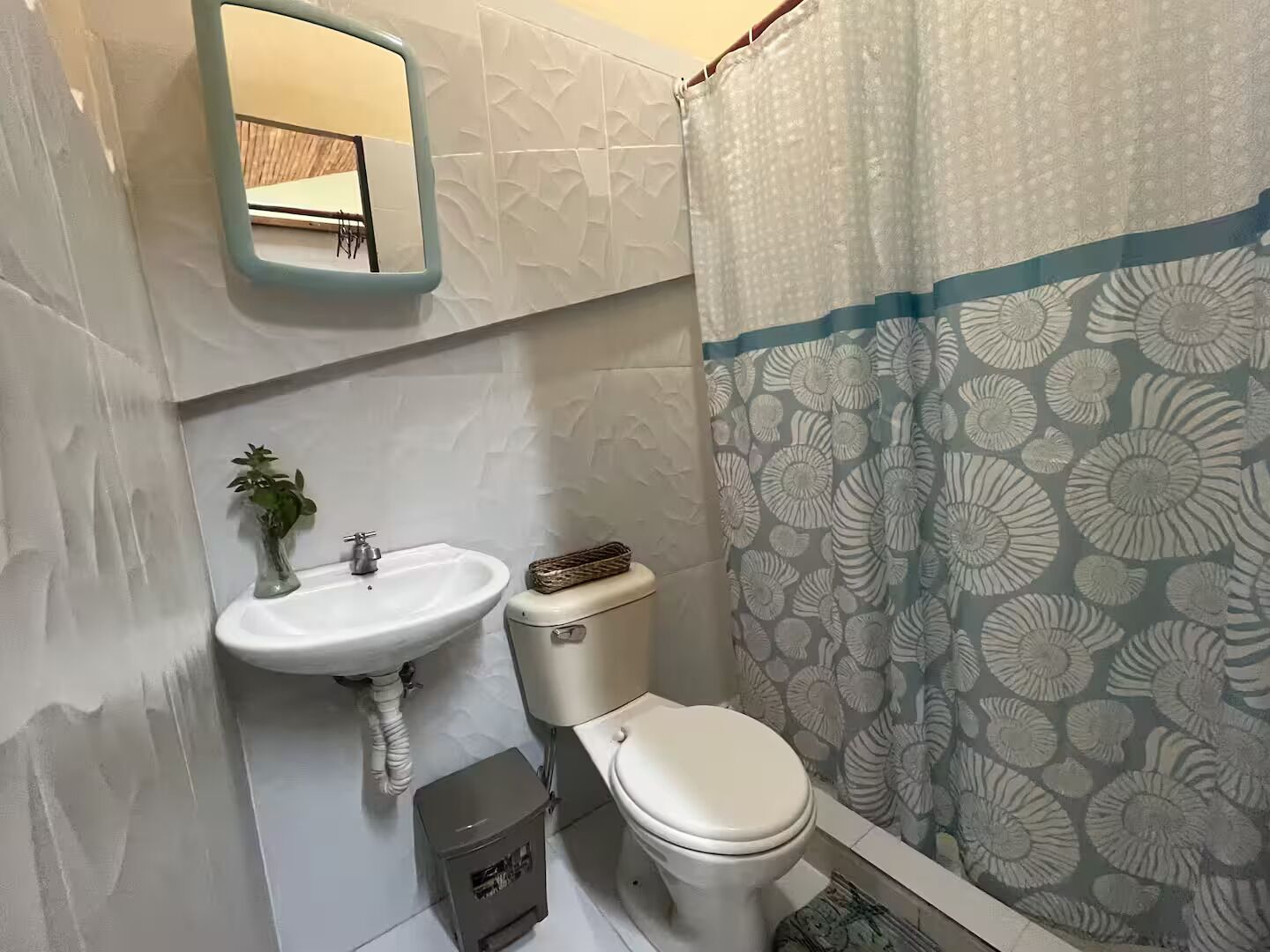 Ein Badezimmer mit weißem Waschbecken, WC und Duschvorhang mit Muschelmuster.