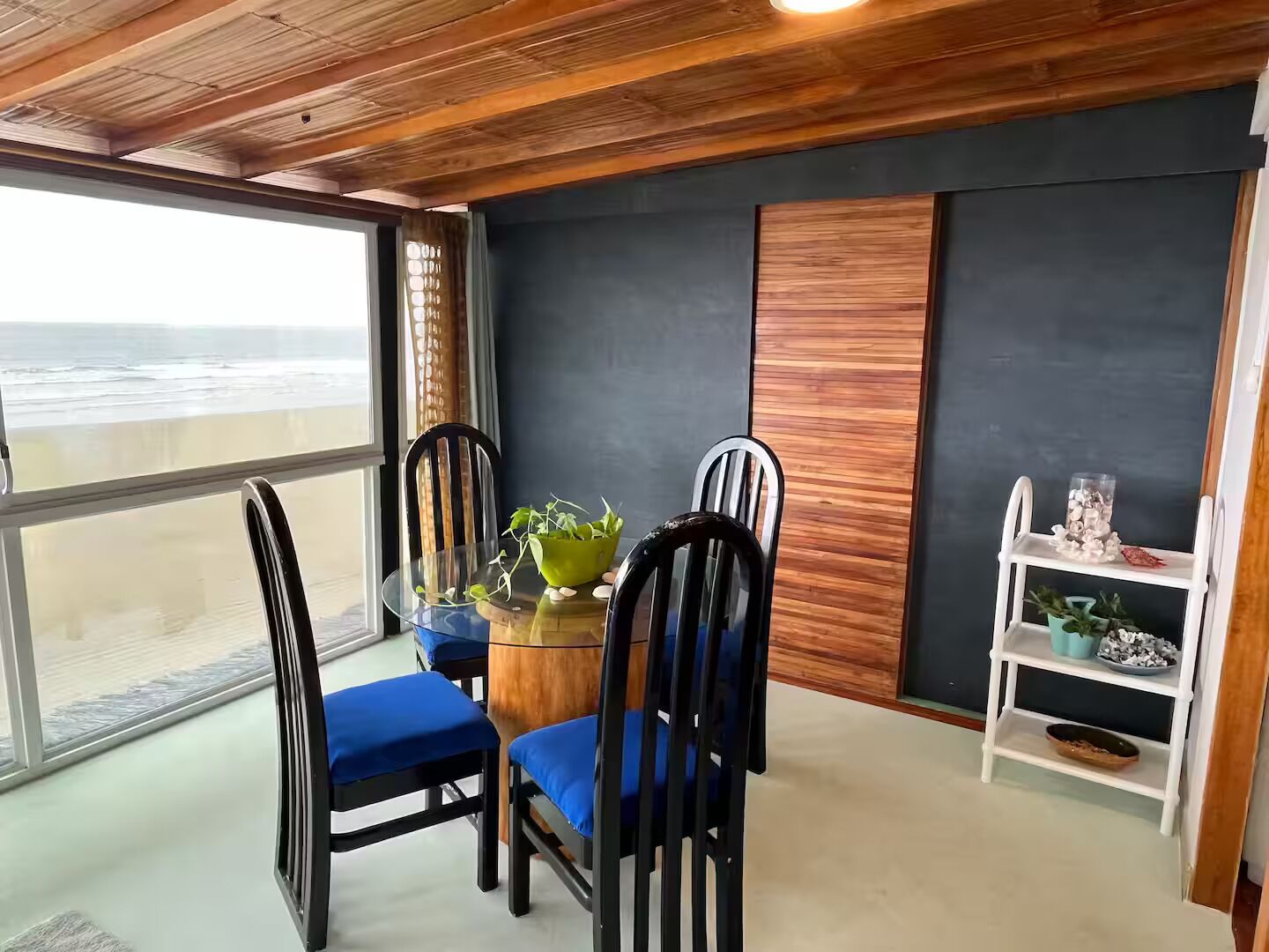 Zona pranzo con tavolo e sedie, vista sull'oceano e uno scaffale con oggetti decorativi.