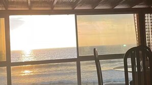 Et værelse ved stranden med havudsigt i solnedgang, med træloft, stort vindue og en stol.