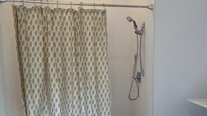 Un baño con cortina de ducha, cabezal de ducha y un estante pequeño.