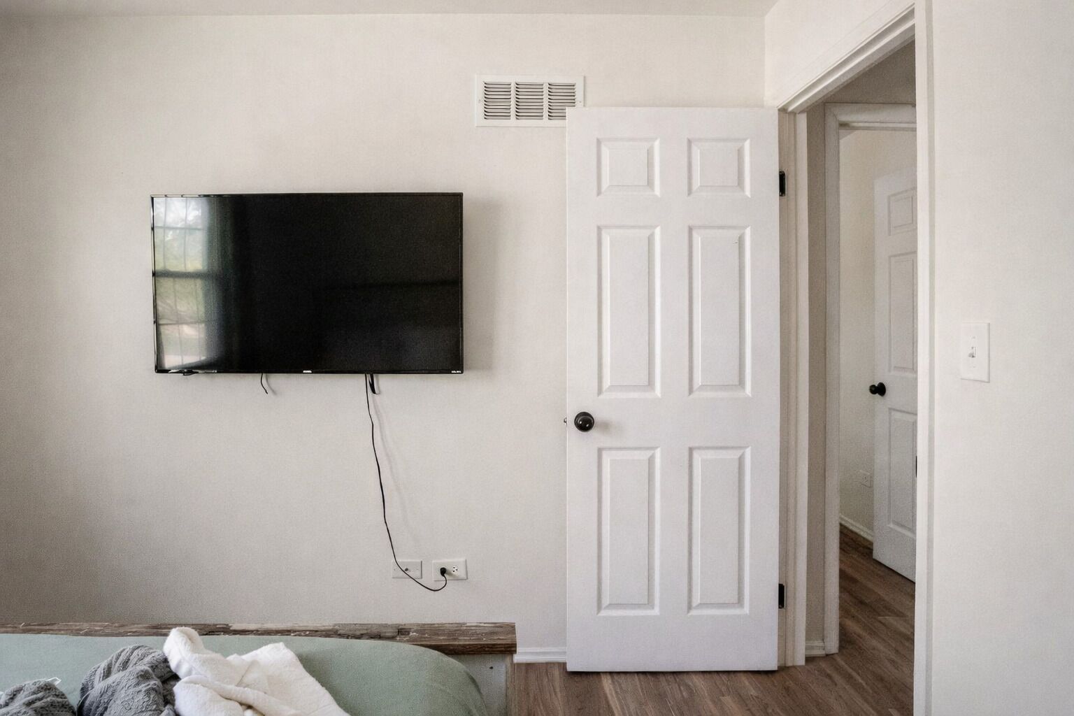 Ein Zimmer mit an der Wand montiertem Fernseher, einer weißen Tür und einer sichtbaren Steckdose.