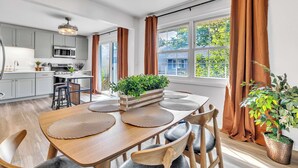 A modern kitchen with grey cabinets, a microwave, and a dining area with a wooden table and chairs. - Modern Spacious  4BR Home Near Chicago • Sleeps 10 • Family & Pets Friendly (Westmont)