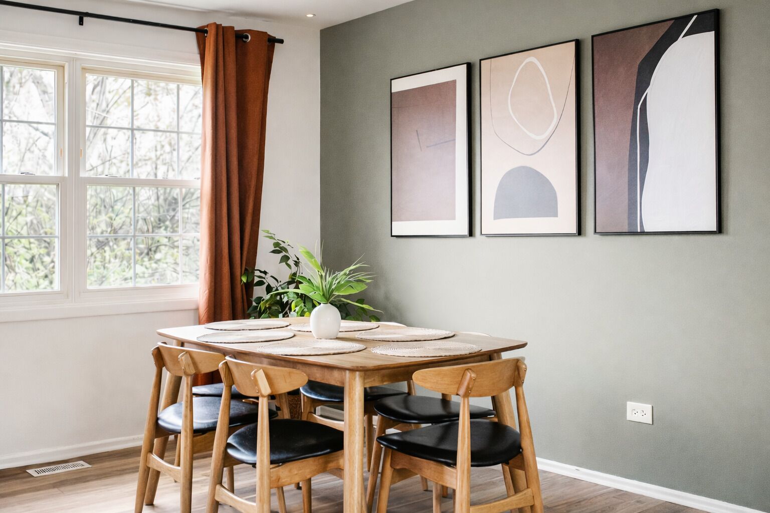 Un comedor con una mesa redonda, seis sillas de madera y tres obras de arte abstracto enmarcadas en la pared.