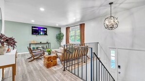 A modern living room with a staircase, a mounted TV, and a chandelier. - Modern Spacious  4BR Home Near Chicago • Sleeps 10 • Family & Pets Friendly (Westmont)