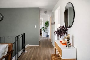 A hallway with a staircase, a wooden bench, a plant, a mirror, and a small table with decorative items.