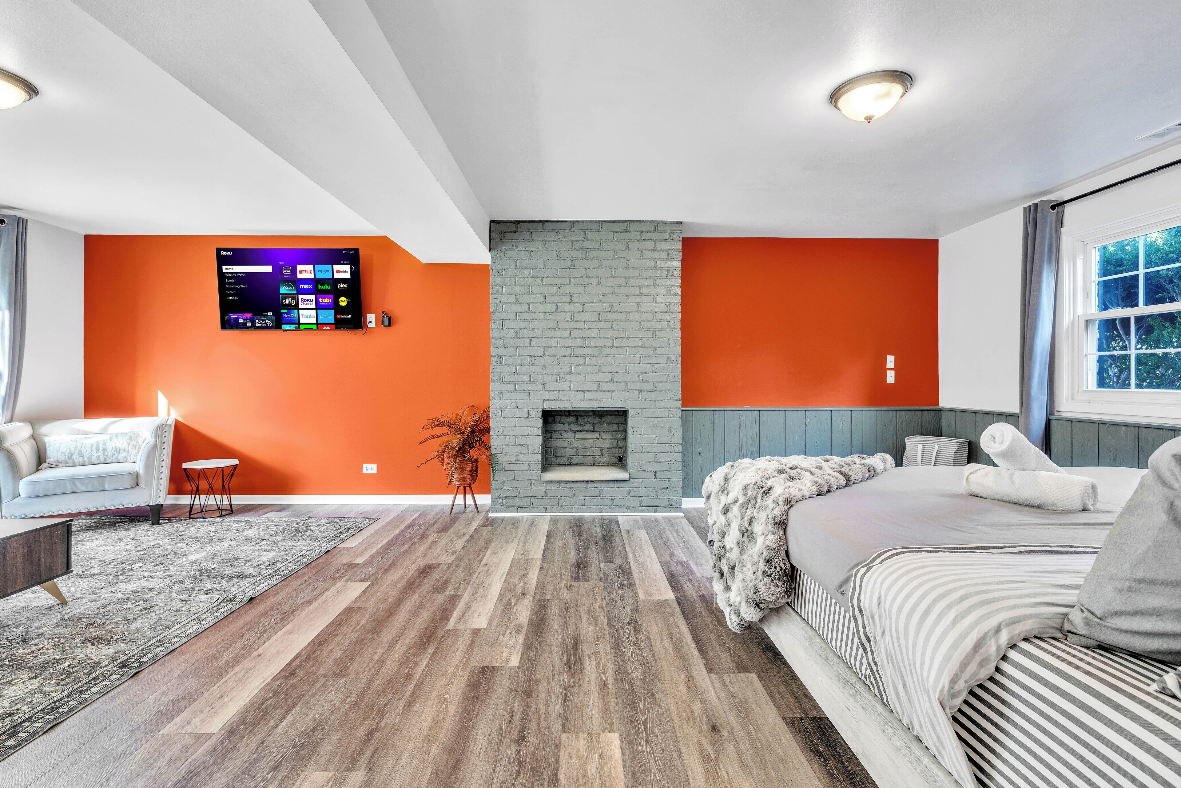 A modern living room with a fireplace, a sofa, a bed, and a flat-screen TV mounted on the wall.