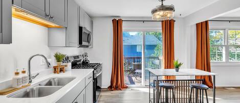 A modern kitchen with a built-in oven, a sink, and a dining area with a table and bar stools.