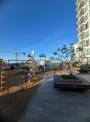 Ein Spielplatz mit Rutschen und Klettergerüsten, eine kleine, blaue Kiosk und ein Gebäude im Hintergrund.