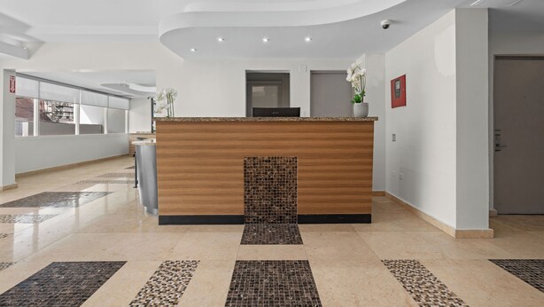 A modern reception area with a wooden counter, a tiled floor, and a view of the hallway. - Near Old San Juan La Placita The Beach (San Juan)