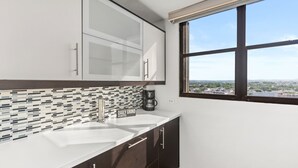 A modern kitchen with two sinks, a coffee maker, and a view of the city through a large window. - Waterside Flat With Garage and Easy Beach Access (San Juan)