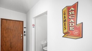 A hallway with a wooden door labeled "101," a "NO PUNYA" sign, and a wall-mounted sign advertising "ARCADE GAMES" for 25 cents. - Otium Beach Walking Distance King Size Bed (San Juan)