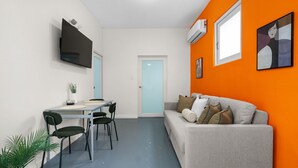 A compact living space with a dining area, a sofa, and a TV mounted on the wall. - Otium Beach Walking Distance King Size Bed (San Juan)