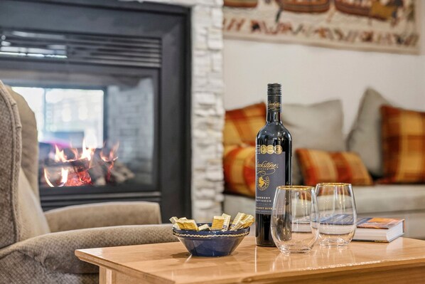 A cozy living room with a fireplace, a bottle of Blackstone wine, glasses, and snacks on a wooden table.