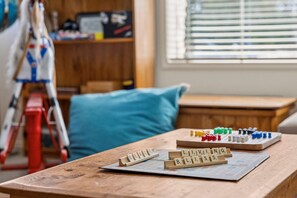 A wooden table with Scrabble tiles spelling out 'BEACH BLISS' and other words, a red ladder, and a blue pillow in a room with a window and a bookshelf in the background. - Beach Living Bliss (Torquay)