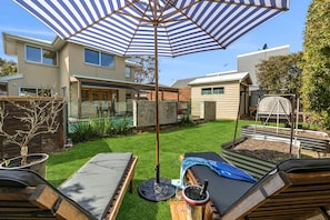 A backyard with a patio area, a pool, and a house.