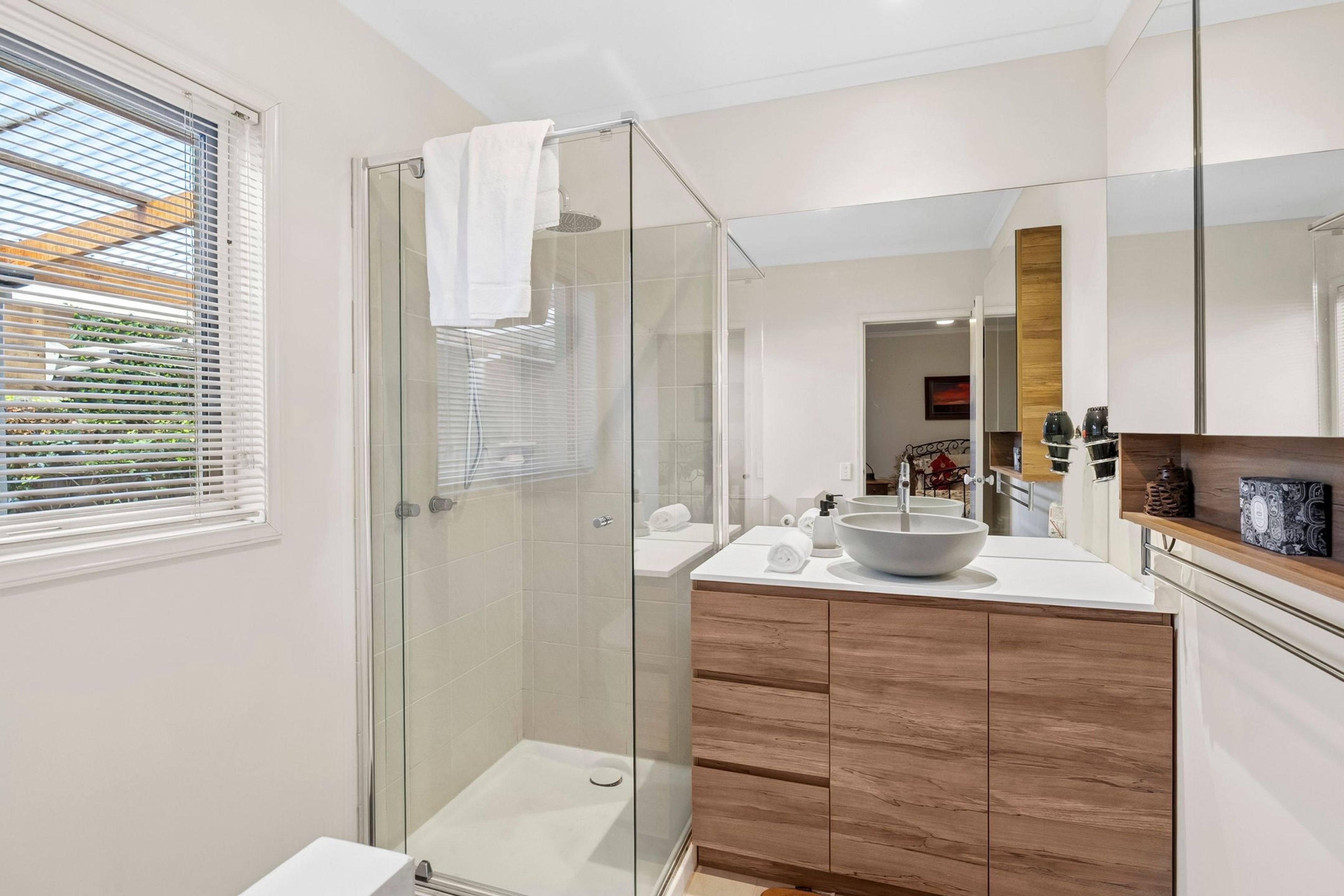 Un bagno moderno con box doccia in vetro, un lavandino bianco dotato di una ampia vasca e mobili contenitori in legno.